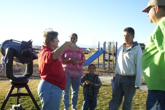 A group of four people, including a child, interacting near a telescope in a playground.
