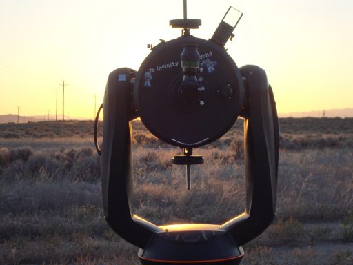 Telescope silhouette against a sunset over a field.