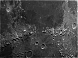 Moon Lunar surface showing craters and rugged terrain in grayscale.