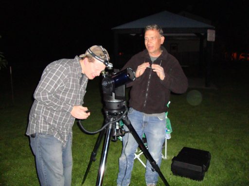 Matt of the Brighton Astronomy Group Two men set up a telescope outdoors at night, one adjusting the device and the other preparing.